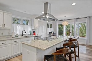 A modern kitchen with white cabinetry, a central island, and a large window providing a view of greenery.