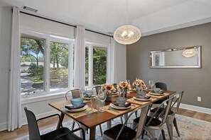 A dining area with a table set for four, large windows, and a hanging light fixture. - Fabulous 3-Bdrm Beach Home, Short Walk from Beach with Beautiful Golf Views (Hilton Head Island)