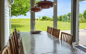 A dining table with chairs, a vase with flowers, and a bowl of fruit.
