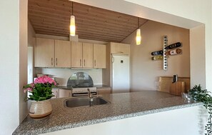 A kitchen with granite countertops, wooden cabinets, a stainless steel sink, a refrigerator, and pendant lights.