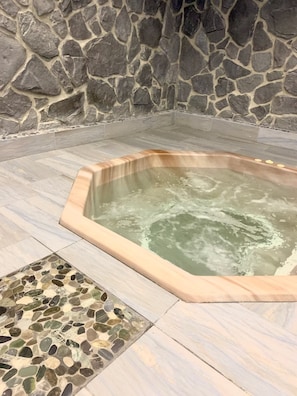Ein Whirlpool vor einer Steinwand, mit Fliesenboden und einer Zone mit Kieselsteinen.