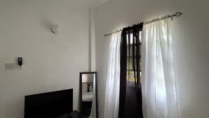 Een slaapkamer met een bed, een dressoir, een spiegel en een raam met dunne gordijnen.