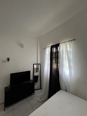 Ein Schlafzimmer mit Bett, Schminktisch, Spiegel und einem Fenster mit durchsichtigen Vorhängen.