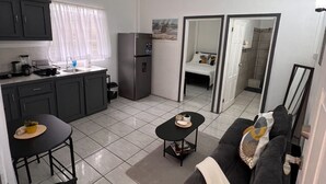 Een knus woongedeelte met een kitchenette, een eethoek met tafel en stoelen, een bank en een grote spiegel die de ruimte weerspiegelt.