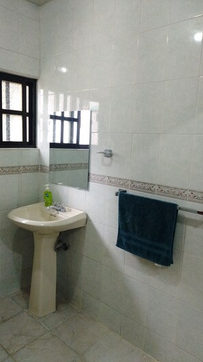 Un baño con lavamanos pedestal, un espejo, un perchero para toallas y una ventana con persianas.