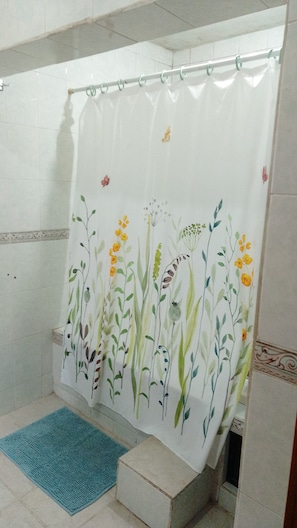 A bathroom with a shower curtain featuring floral patterns, a blue bath mat, and a tiled floor. - CASA MEXICANA (Mexico City)