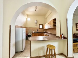 A kitchen with an island, a refrigerator, a stove, wooden cabinets, and a window.
