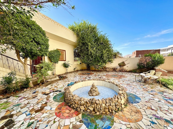 A courtyard with a mosaic floor, a stone fountain, and surrounding greenery.