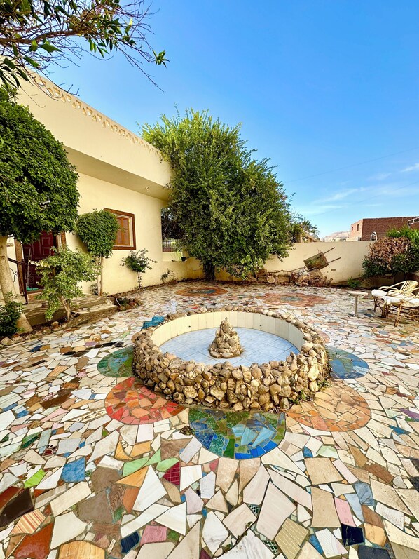 A courtyard with a mosaic floor, a central fountain, and surrounding greenery.