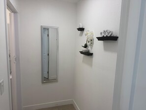 Un pasillo con espejo, paredes blancas y estantes negros decorados con objetos.