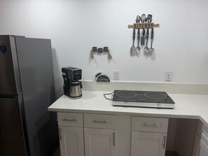 Una cocina con refrigerador, cafetera, placa de inducción y utensilios en la pared.