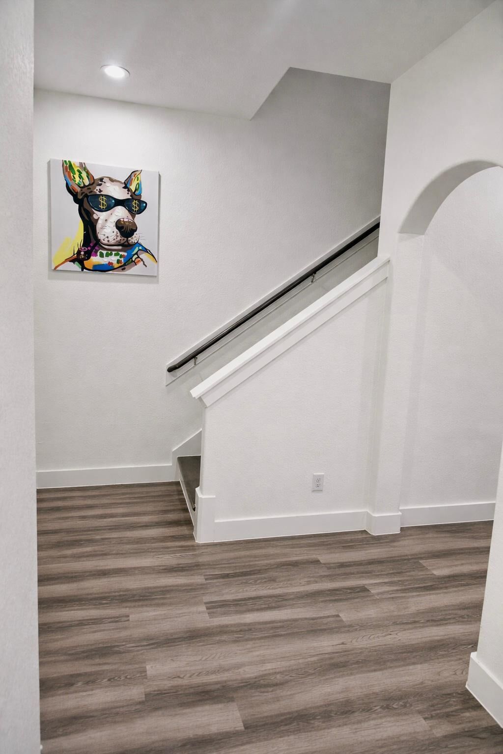 Een trap met een witte leuning die uitkomt op een plateau, een houten vloer en een kunstwerk van een hond aan de muur.