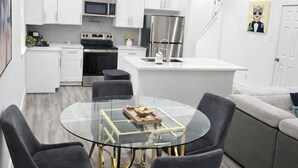 A modern kitchen with white cabinets, a stainless steel refrigerator, and a glass dining table with chairs. - Comfy Modern Getaway10mins from downtown (Houston)