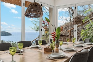 A dining table set with plates, glasses, and a vase with flowers, overlooking a scenic view of the sea. - Villa Casa Zula Sayulita with pool, palapa, and breathtaking ocean views (Sayulita)