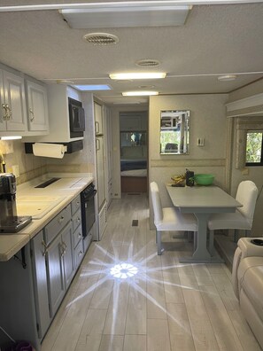 Una cocina compacta para vehículos recreativos, con microondas, lavamanos y zona de comedor.