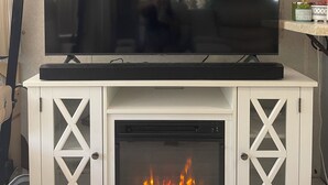 Ein Kamin mit einem Fernseher darauf, eine weiße Vitrine mit Glastüren und eine Steinwand darüber.