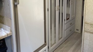 Ein Flur mit einem weißen Kühlschrank, einer Mikrowelle und einem Herd auf der linken Seite. Auf der rechten Seite befinden sich weiße Schränke mit Glastüren.