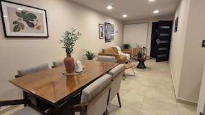 Un coin repas avec une table en bois, des chaises à revêtement gris, un vase avec des plantes et, au mur, des œuvres d’art encadrées sur le thème de la botanique.