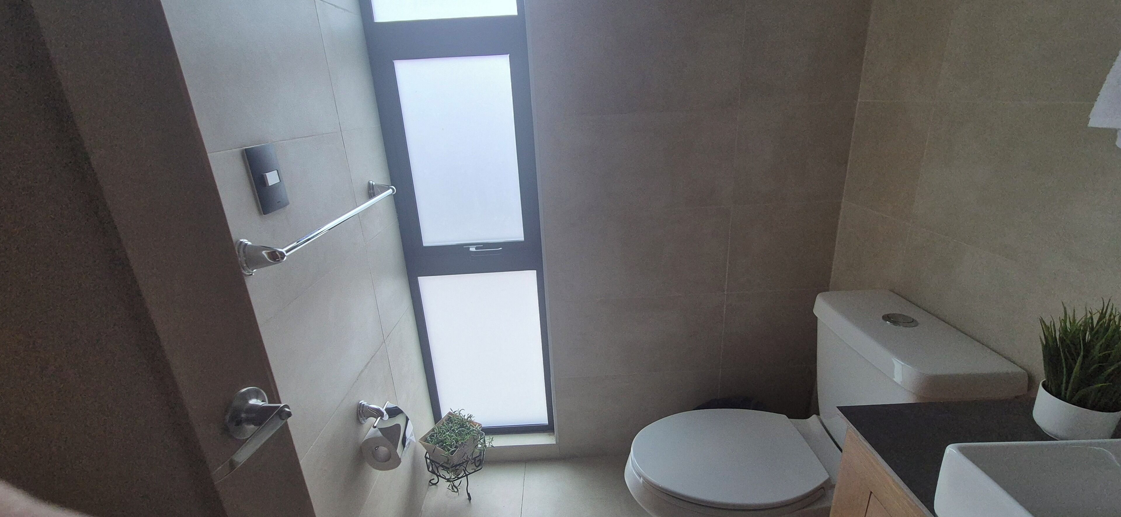 A small bathroom with a toilet, a sink, a window, and a shower area.