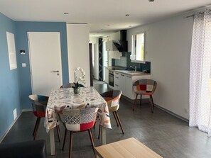 A dining area with a table and chairs, a kitchen in the background, and a door leading to another room. - New house - 6 guests, near the town (Jard-sur-Mer)