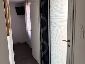 Un pasillo con una puerta, un televisor fijado a la pared y una cortina estampada.