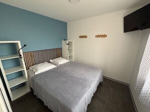 A bedroom with a bed, a white shelving unit, a TV mounted on the wall, and a patterned window. - New house - 6 guests, near the town (Jard-sur-Mer)