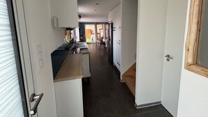 Een smalle gang met een keuken aan de ene kant, een eethoek in het midden en een deur naar een andere kamer aan de andere kant.