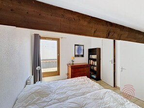 Ein Schlafzimmer mit Bett, Kommode, Bücherregal und einer Tür zu einem anderen Raum.