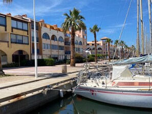 A marina with boats docked, a building with arched windows, and palm trees. - Apartment with AC, port, pets welcome - 4 guests (Port Leucate)