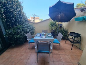 En patio med et bord dækket til to, stole, grill og en stor parasol.