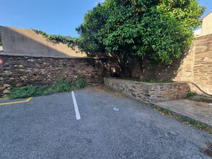 Ein Parkplatz mit Steinmauer und Baum mit grünen Blättern.