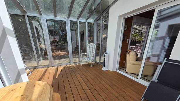 Een houten terras met glazen wanden, een stoel en een bank.