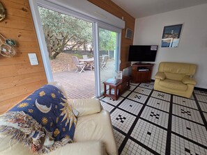 A living room with a sofa, a yellow armchair, a TV, and a view through a glass door to an outdoor patio. - Spacious house near the beach - 8 guests (La Tranche-sur-Mer)