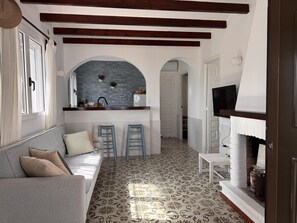 A cozy living area with a sofa, two bar stools, a fireplace, and a kitchen with a blue backsplash. - Beachfront house with stunning views - 4 guests (Denia)
