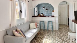 A room with a sofa, two bar stools, a kitchen area with a blue backsplash, and patterned flooring. - Beachfront house with stunning views - 4 guests (Denia)