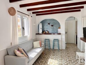 A room with a sofa, two bar stools, a kitchen area with a blue backsplash, and patterned flooring. - Beachfront house with stunning views - 4 guests (Denia)