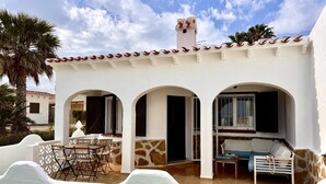A white building with a tiled roof, three arched doorways, a patio with a table and chairs, and a small window. - Beachfront house with stunning views - 4 guests (Denia)