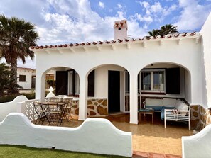 A white building with a tiled roof, three arched doorways, a patio with a table and chairs, and a small window. - Beachfront house with stunning views - 4 guests (Denia)