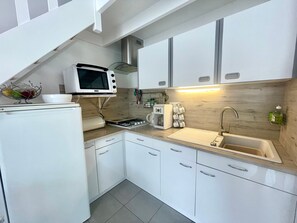 Een kleine keuken met witte kastjes, een magnetron, een fornuis en een spoelbak.