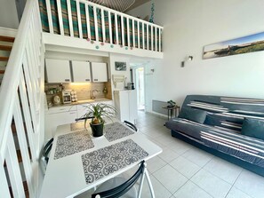 Een ruimtelijke zithoek met kitchenette, eethoek en een bank.