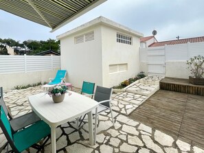 Een terras met een witte tafel, stoelen, een plant in pot en een kleine tuin.