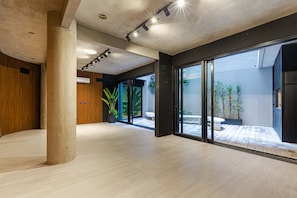 Ein großzügiger Innenraum mit Beton Decke, großen Fenstern und Blick auf eine Außenpatio-Terrasse.