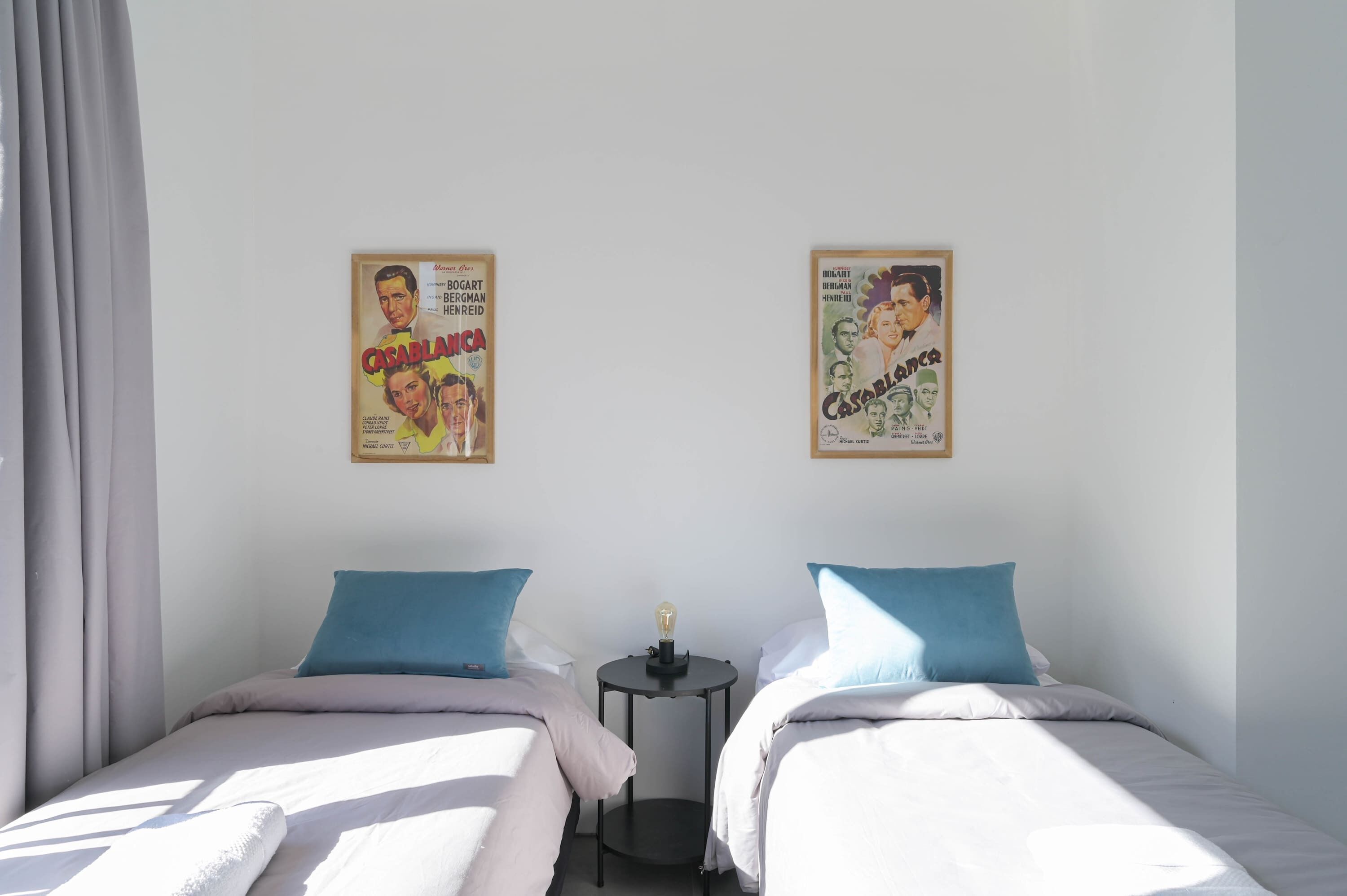 Une chambre avec deux lits, une petite table et deux affiches au mur.