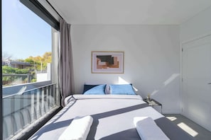 A bedroom with a large window, a bed with white linens, a nightstand with a lamp, and a framed abstract artwork on the wall. - MOT Rentals + Black Ravignani 2C - 2 Bd Palermo Hollywood (Buenos Aires)