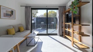 En moderne stue med sofa, bord, bogreol og en skydedør til et udendørs område.