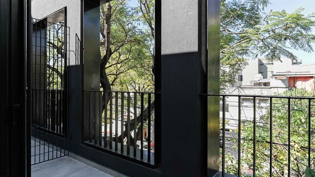 Ein Balkon mit Metallgeländer, Blick auf Bäume und ein Gebäude im Hintergrund.