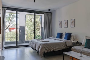 A bedroom with a large sliding glass door leading to a balcony, a bed with a grey duvet, a bedside table with a lamp, and three framed pictures on the wall. - MOT Rentals + Black Ravignani 2A - 3 pax Loft Palermo Hollywood (Buenos Aires)