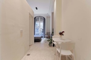 A narrow hallway with a bed, a dining table with chairs, and a potted plant. - Leonardo Da Vinci Aparts 1D by MOT Rentals (Buenos Aires)