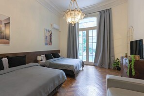 Habitación de hotel con dos camas, una araña, un televisor y una ventana con cortinas.