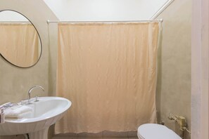 Un baño con lavamanos, espejo, inodoro y cortina de ducha color beige.